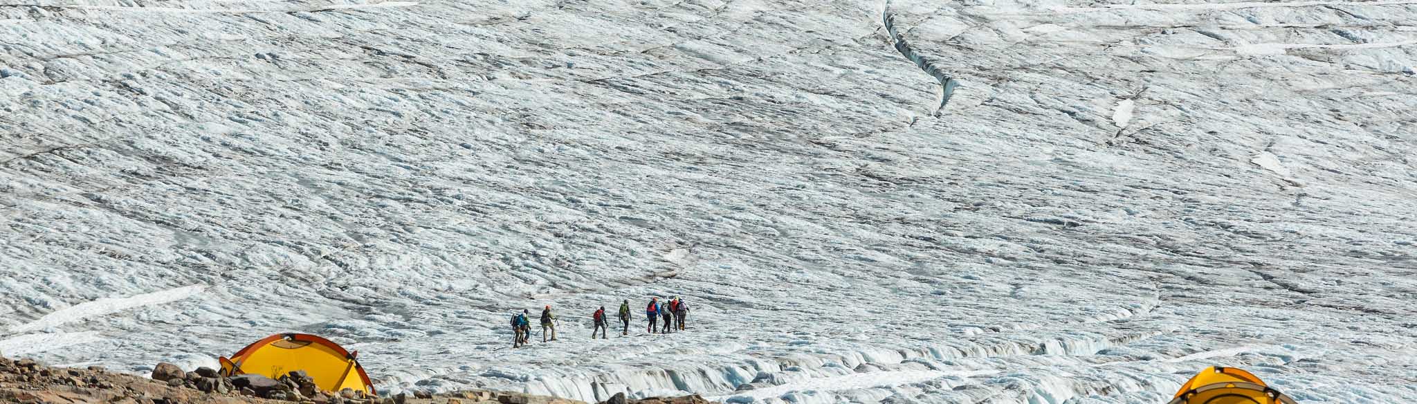 A group of hikers made to look miniscule by a giant glacier